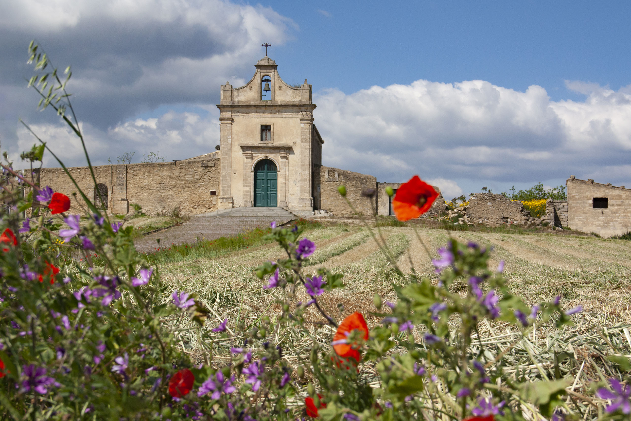 La facciata della chiesa con in primo piano papaveri rossi e fiori viola
